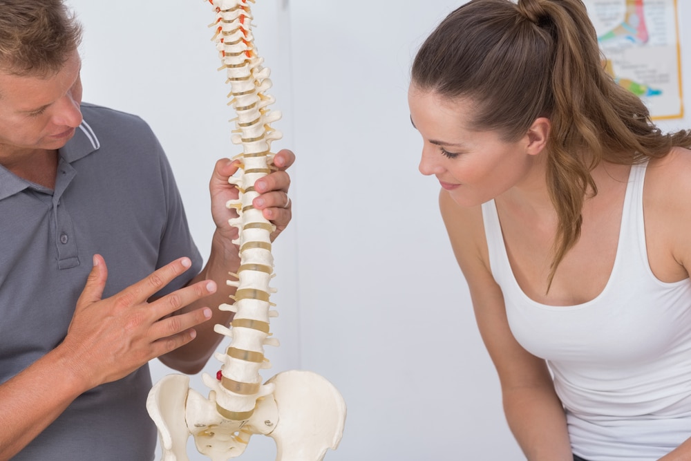 Osteopath or chiropractor explaining to female patient with model spine