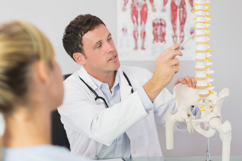 Young doctor with model spine explaining to patient