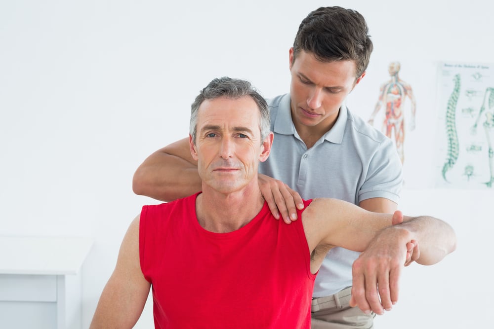Osteopath or chiropractor assessing man for shoulder pain or frozen shoulder