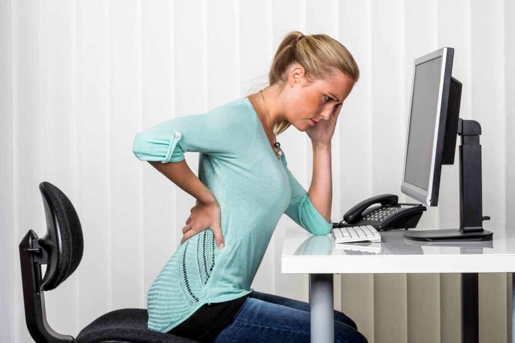 female at desk holding back in pain